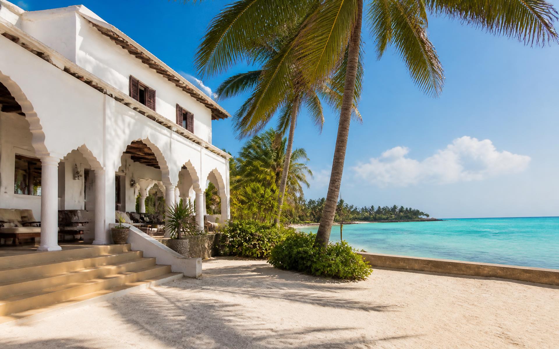 Whitewashed coastal building with arches beside palms and turquoise water